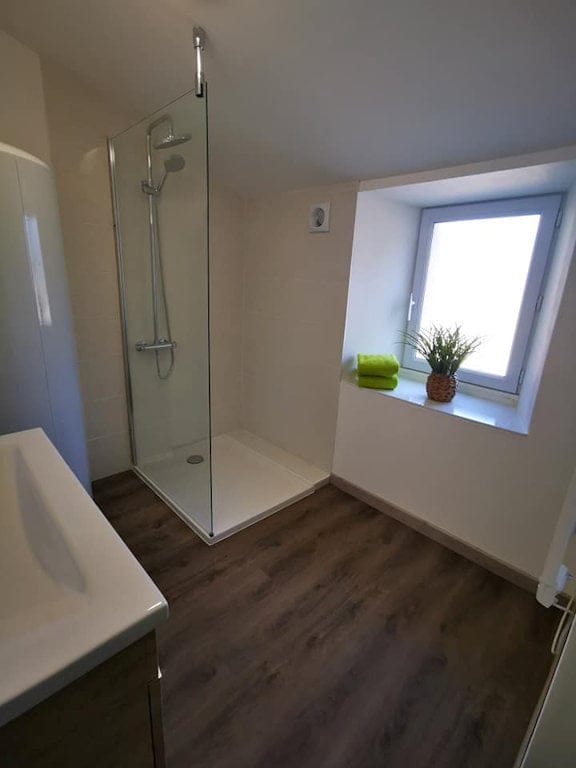 Salle de bain moderne du Gîte Le Graizeau avec une douche à l'italienne, des finitions élégantes et une fenêtre offrant une lumière naturelle.