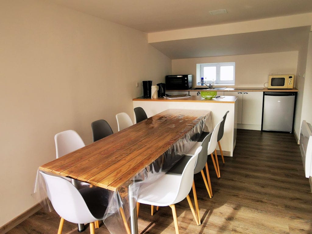 Salle à manger lumineuse du Gîte Le Graizeau avec une grande table en bois et une cuisine équipée en arrière-plan.