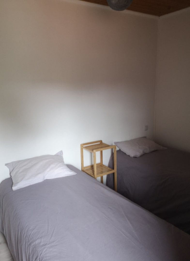Chambre avec lits une personne une place, draps gris et oreillers blancs.
